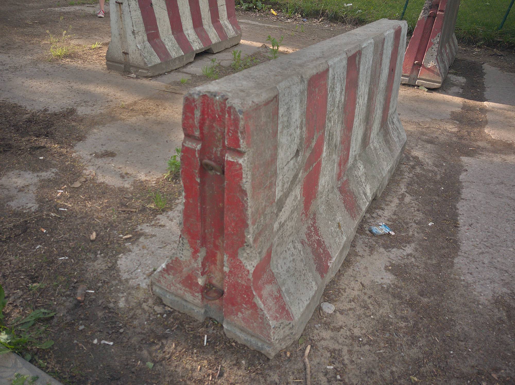 A painted concrete road barrier photographed on location, with a second barrier and a steel one behind it.